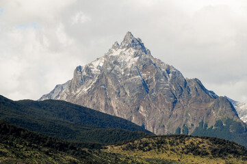 Fototapeta premium Mountain peaks covered with snow and hills with grass and vegetation