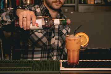 Fototapeta na wymiar Bartender adding grenadine syrup to glass with Tequila Sunrise cocktail decorated with orange and straw