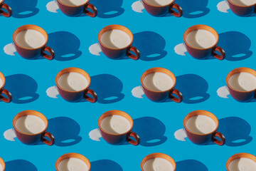 Continuous pattern of a brown ceramic cup with spilled milk on a blue background
