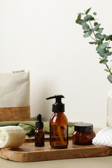 Brown amber glass cosmetic bottles on wooden tray on table with cosmetic bag and eucalyptus. Luxury...