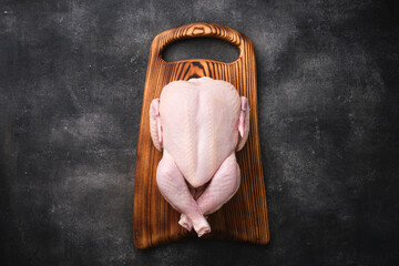 Whole raw chicken on wooden board on dark background. Preparing raw chicken. Top view. - 498894455