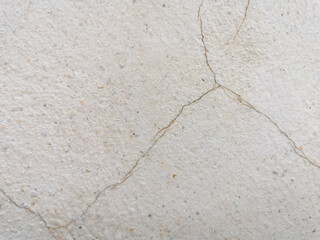 Beige cracked cement with fine gravel surface. Ferruginous cracks pattern on plaster wall. Old stucco wall with marble grains and rusty cracks