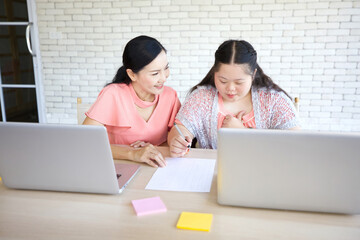 down syndrome teenage girl and her teacher studying and writing about math on paper with laptop computer for education