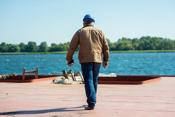 a male docker in a helmet walks along the deck of a river barge moored in the port