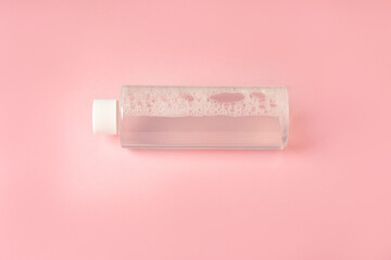 Бутылка мицеллярной воды лежит на розовом фоне
