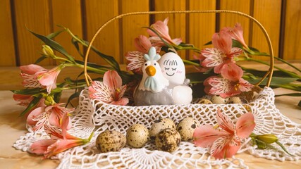 Easter basket with quail eggs and pink flowers. Decorative chicken with egg with a smile. Pink alstroemerias around.