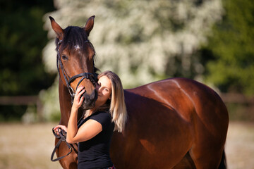 Obraz premium Brown horse with a young woman in portrait in front of a flowering bush, detail of the horse's body and the woman's upper body..