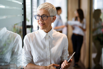 Confident stylish european mature business woman standing at workplace.