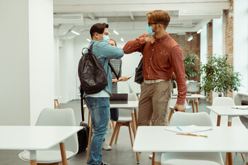 Male students in facial masks greeting bumping elbows