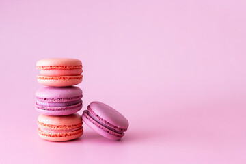 Pink and lilac macaroons lie in a stack on a light pink table. Pale pink background, space for text