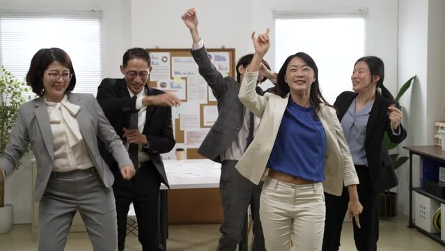 group of happy Asian businesspeople wearing suit are partying together with fun dance moves for celebration at workplace