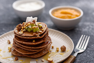 lean chocolate pancakes with honey, nuts on plate with fork on gray background, healthy delicious breakfast snack