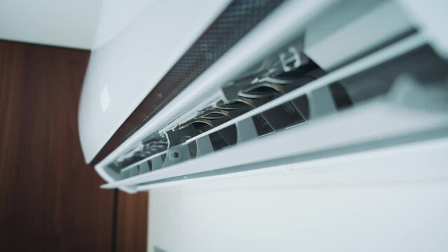 Close-up shot indoor unit air conditioning in room attached on wall. Flow of cold, frosty air, cooling house. Modern technologies. Turns on wing goes down, blinds are opened, drives cold air. Video 4k