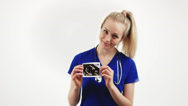 Cheerful caucasian blonde female doctor holding prenatal ultrasound screening and smiling. Medium studio shot over white background. High quality 4k footage