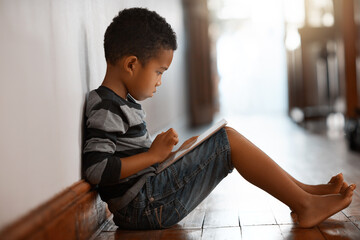 Theres an app for everyone. Full length shot of a young boy using his digital tablet while sitting on the floor at home. © Nikish Hiraman/peopleimages.com
