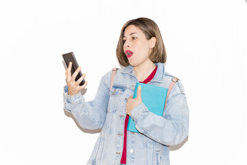 Young caucasian female student isolated on a white background surprised by the video she is watching on her mobile phone, while holding a book with the other arm. Lifestyle, spring.