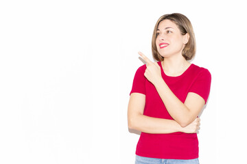 Horizontal photo of an adorable young woman dressed in casual pink clothing pointing to the empty blank space in the background, looking at what is pointed out.