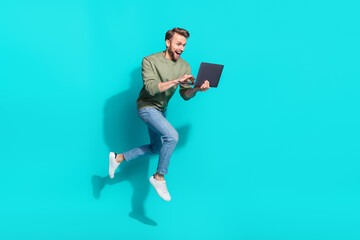 Full length photo of millennial blond guy jump type laptop wear sweater jeans shoes isolated on turquoise background