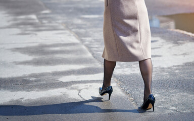 Woman legs in tight shiny pantyhose and black high heels shoes walking on asphalt road. Fashion...