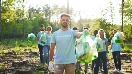 Portrait of caucasian man looking at the camera and posing with plastic bag full of rubbish outdoor...