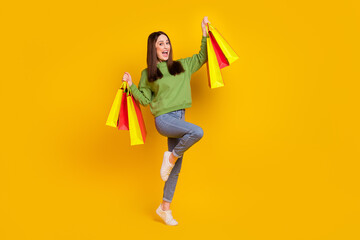 Full length body size view of attractive cheerful woman holding bags dancing isolated over bright yellow color background