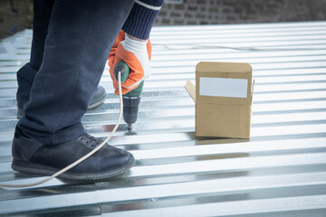 Man installing metal sheet roof by electrical drilling machine.