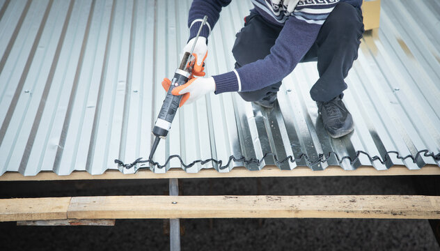 Worker using glue gun with adhesive to fix the metal steel on the roof.