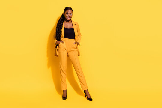 Full size photo of good millennial lady stand wear suit stilettos isolated on yellow color background