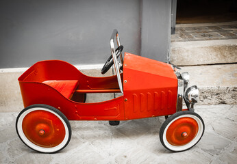 Red vintage toy car near entrance to the house. Side view. Black white sepia red toned photo.