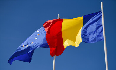Flags of Romania and EU European Union winding against blue sky background