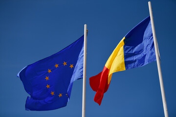Flags of Romania and EU European Union winding against blue sky background