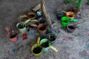 Plastic containers on a studio floor hold brushes and paint used in the dye process of batiking on the island of Bali, Indonesia.