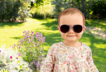 childhood and people concept - happy little baby girl in sunglasses over summer garden background