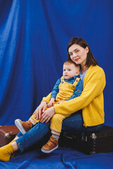 A young mother sits with a 3-year-old son in her arms, family relationships with a child. Children's education. Mom with son on a blue background