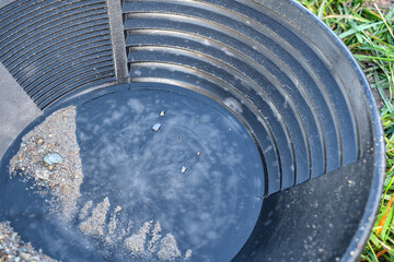 Gold panning in Germany with small gold flakes in a black pan.