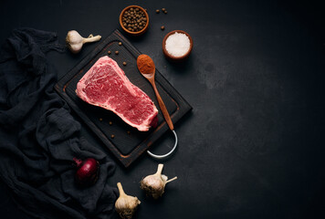 Raw juicy piece of beef meat on the bone lies on a wooden cutting board, spices for cooking on a...