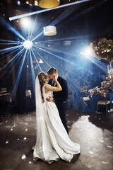 Kiss of newlyweds on first wedding dance and. Just married couple dancing in darkness. Groom holds bride's hand dancing with her in the middle of restaurant. Happy couple and their first dance