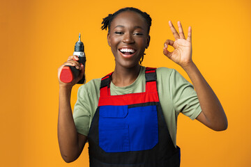 Black African American female model in uniform holding a screwdriver repair tool against yellow...