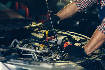 Car mechanic checking oil level in a mechanical workshop