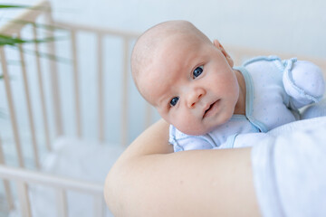 a newborn baby boy in his mother's arms near the crib at home, parental love and care for the baby in the first days after birth