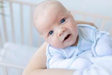 a newborn baby boy in his mother's arms near the crib at home, parental love and care for the baby in the first days after birth