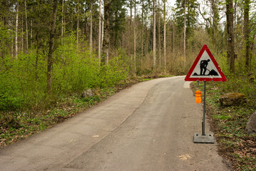 Road works warning road sign on a dirt road in the forest. Day time, no people