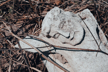 A piece of toppled stone crucifix sculpture on the ground at abandoned ancient cemetery. Broken...