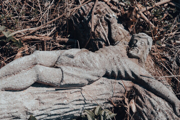 Stone crucifix sculpture on the ground of abandoned ancient cemetery. Broken tombstone at the old churchyard. Cemetery vandalism and headstone repair concept
