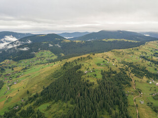 Green slopes of Ukrainian Carpathian mountains in summer. Cloudy morning, low clouds. Aerial drone view.