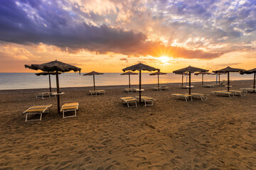  empty beach during beautiful sunrise or sunset with chaise loungues and nice umbrellas with blue sea