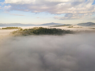 Flight over fog in Ukrainian Carpathians in summer. Mountains on the horizon. A thick layer of fog covers the mountains with a continuous carpet. Aerial drone view.