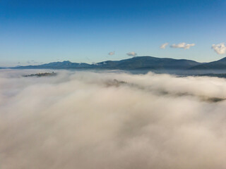 Sunny morning in the foggy Carpathians. A thick layer of fog covers the mountains. Aerial drone view.
