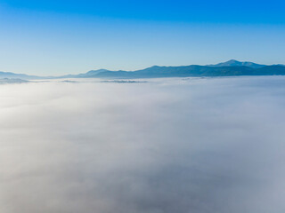 Obraz premium Flight over fog in Ukrainian Carpathians in summer. Mountains on the horizon. A thick layer of fog covers the mountains with a continuous carpet. Aerial drone view.