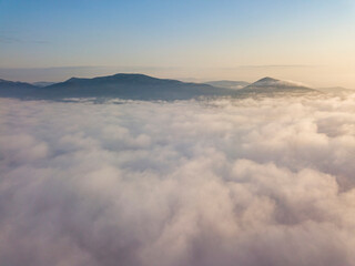 Flight over fog in Ukrainian Carpathians in summer. Mountains on the horizon. Aerial drone view.